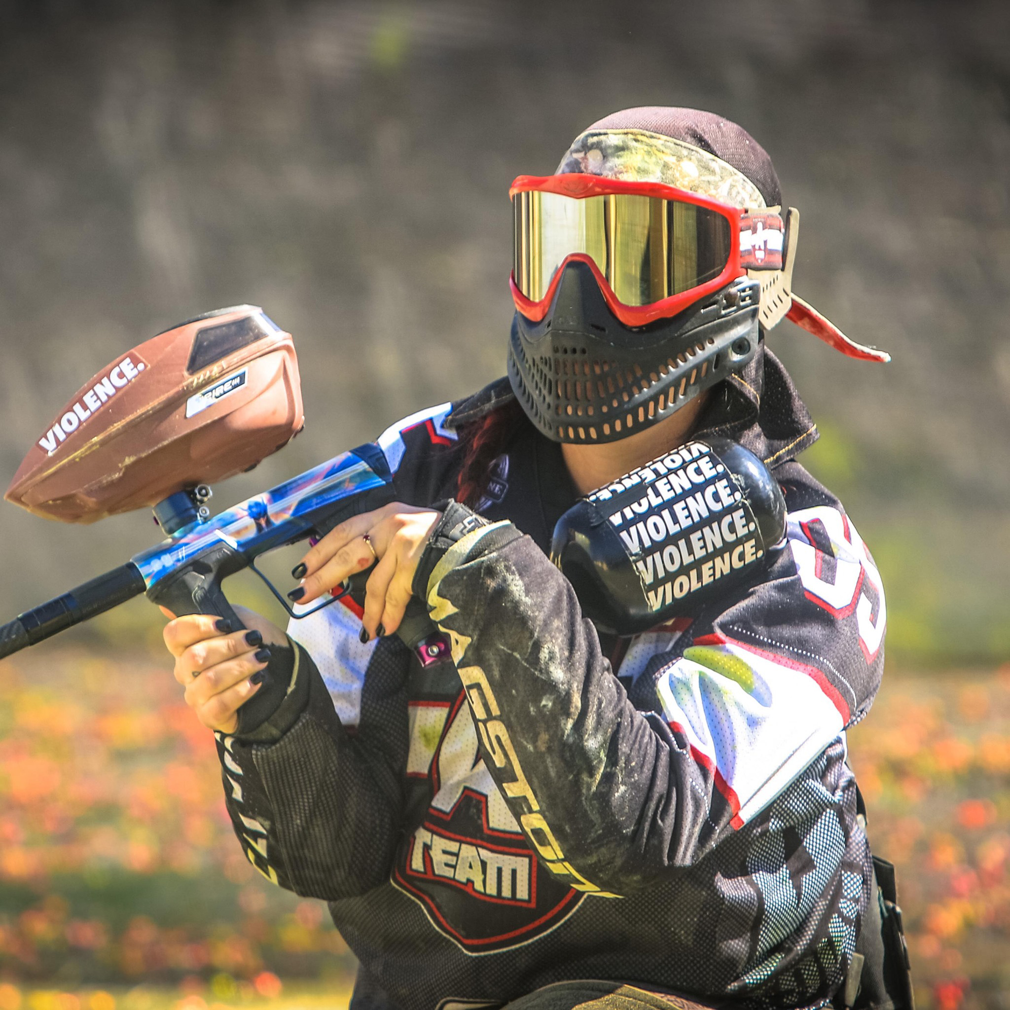 Paintballer in full gear standing in grass with cloudy background and Cousins Paintball logo.